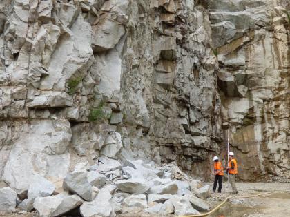 Blick auf mächtige, stark zerfurchte Steinbruchwände. Das Gestein, von dem links vorne größere Blöcke aufgehäuft sind, ist hellgrau bis dunkelgrau, rechts auch bräunlich grau gefärbt.
