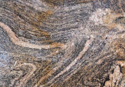 Anatektisch überprägter und gefalteter Paragneis Nahaufnahme einer Gesteinsoberfläche mit wellenartigen Mustern in rosa, grau und dunkelgrau. Dazwischen treiben rötlich braune Schlieren.