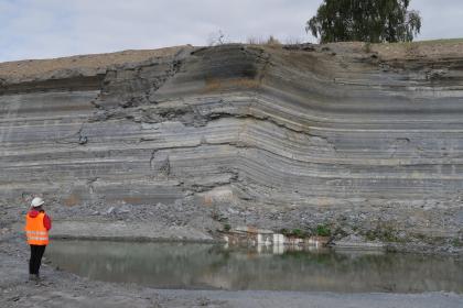 Posidonienschiefer-Formation, Abbauwand im Steinbruch Dormettingen (Zollernalbkreis) Gezeigt wird die Abbauwand eines Steinbruches. Die dünnen, von hellgrau über dunkelgrau bis braun gefärbten Lagen machen rechts der Bildmitte einen wellenförmigen Knick.