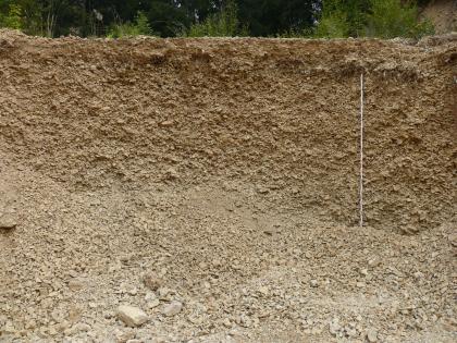 „Albschutt“ in der Kiesgrube Deilingen Teilansicht einer Kiesgrube. Zu sehen ist eine rötlich braune, etwa drei Meter hohe Wand sowie im Vordergrund gehäufter Kies und Schutt.