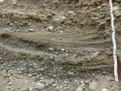 Detail von Grobkieslagen mit auskeilenden Sandlinsen Großaufnahme von grob- bis feinkörnigen Kieslagen. In der Bildmitte liegt eine Sandschicht dazwischen. Rechts außen ist ein Maßstab angelehnt.