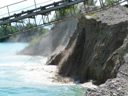 Kiesgrube mit Nass- und Trockenabbau Blick auf die „Küste“ eines Baggersees, mit rechts aufsteigenden Kiesbänken. Links oben ist das Gitter eines Förderbandes zu erkennen.