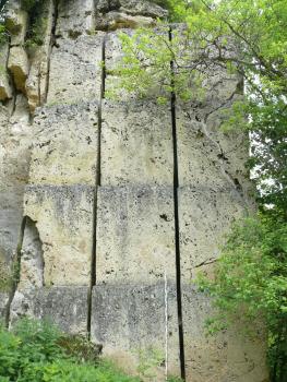 Kalktuffwand mit Abbauspuren durch eine Schrämsäge Blick auf eine steil aufragende, hellgraue Gesteinswand. Horizontale, durchgehende Schnitte im Gestein deuten auf Sägearbeiten hin. Die Frontseiten des Gesteins sind ebenfalls bearbeitet.