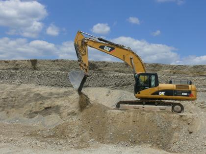 Trockenkiesabbau in einer Kiesgrube bei Orsingen Das Bild zeigt den Kiesabbau in einer Grube. Auf einer erhöhten, flachen Halde rechts vorne arbeitet ein gelber Bagger. Dahinter die hellen Wände der Grube.