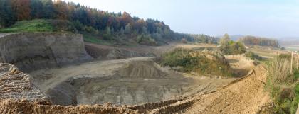 Übersicht des Abbaugebiets einer Kies- und Sandgrube bei Stockach (RG 8120-1) Übersichtsbild einer Kies- und Sandgrube mit hohen Abbauwänden links, niedrigen und offenen Wänden rechts sowie Abraumhalden in der Bildmitte. Im Hintergrund links steht Wald an.