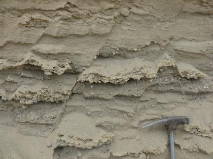 Gestörte Kies- und Sandlagen Gestörte Kies- und Sandlagen. Das anstehende Gestein ist hellgrau. Am rechten unteren Bildrand befindet sich der Kopf eines Geologenhammers.