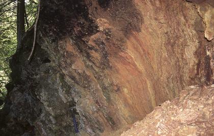 Frischer Ausbruch im Wallsinter Blick auf eine nach innen gewölbte Gesteinswand, die rechts mit rötlichen und hellbraunen Farben beginnt, nach links hin jedoch immer dunkler und im äußeren Hangbereich fast schwarz ist.
