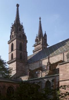 Das Foto zeigt zwei Türme sowie weitere Bauten einer Kirche. Die Türme stehen links und mittig und sind wie der Rest der Kirche aus rötlichem Gestein gebaut. Das Dach des Hauptschiffes hat ein rautenförmiges Muster.