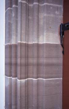 Mauerquader an der evangelischen Kirche in Schopfheim Blick auf die Einfassung einer Tür mit rötlich grauen, vertikale Furchen aufweisenden Mauersteinen.