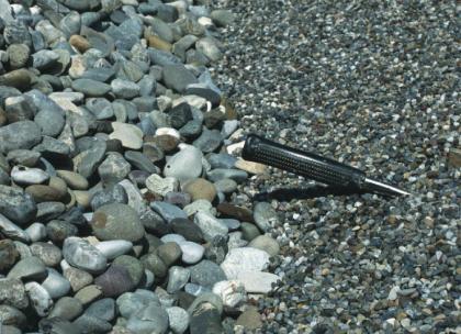 Klassierung in Feinkies und Grobkies Nahaufnahme von grobem Kies links und feinkörnigem, dunkelgrauem Kies rechts. Der Griff eines Hammers im Feinkies zeigt die Größenverhältnisse an.