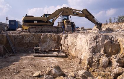 Blick in den Neuaufschluss bei Sonderbuch Blick auf eine Ecke eines flachen Steinbruchs mit gelblich grauem Gestein. Auf der oberen Ebene sind Bagger und Schaufellader im Einsatz.