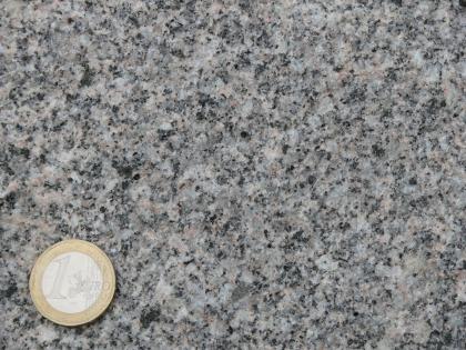 Graue Varietät des Malsburg-Granits Detailaufnahme eines gräulichen Gesteins. Neben den häufigen grauen Kristallen, finden sich auch etwas hellere und kleine schwarze Kristalle im Gestein. Links unten befindet sich eine 1-Euro-Münze als Maßstab.