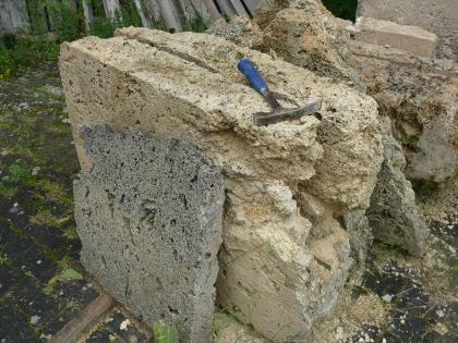 Gesägte Kalktuffplatten im Steinbruch Bärenthal Das Bild zeigt mehrere Gesteinsplatten, seitlich, unten und oben gesägt, vorne unregelmäßig gebrochen. Die Platten sind teils grau, teils rötlich bis gelblich und verschieden dick. Ein Hammer liegt obenauf.