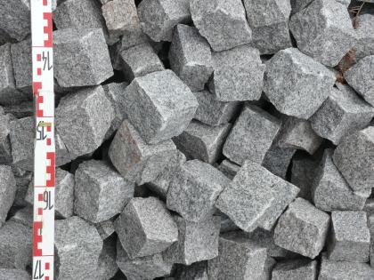 Pflastersteine aus Seebach-Granit Unregelmäßig durcheinander gewürfelte, mittelgraue Pflastersteine. Am linken Bildrand befindet sich ein Maßstab.