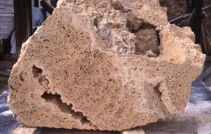 Frisch angeschnittener Block am Tuffsteinwerk Bärenthal Größerer angeschnittener Gesteinsblock mit rötlich brauner Farbe, unregelmäßiger Form, kleineren Lufteinlässen und größeren Hohlräumen oben rechts und unten links.