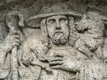 Herz-Jesu-Kirche in Göschweiler: Ausschnitt aus dem Tympanon Detailaufnahme eines aus grünlich grauem Gestein gefertigten Reliefs. Das Relief stellt einen Schäfer mit Hirtenstab dar, der ein Schaf auf der Schulter trägt.
