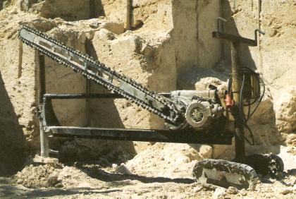 Kalktuffabbau der Fa. Beck bei Bärenthal: Schrämsäge zum Kalktuffabbau Das Foto zeigt eine große Säge, mit Kettenantrieb und auf einem Fahrgestell montiert. Die Säge steht vor einer gelblichen Steinbruchwand mit senkrechten, stufigen Einschnitten.