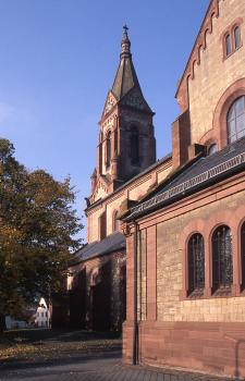 Kirche St. Alban in Hardheim, das Bruchsteinmauerwerk besteht vorwiegend aus grauem Hardheimer Muschelkalk Das Foto zeigt eine Kirche mit Turm in der Bildmitte sowie seitlichem Anbau rechts. Das Mauerwerk besteht aus gelblich grauen Steinen, Einfassungen und Sockel sind rötlich braun.
