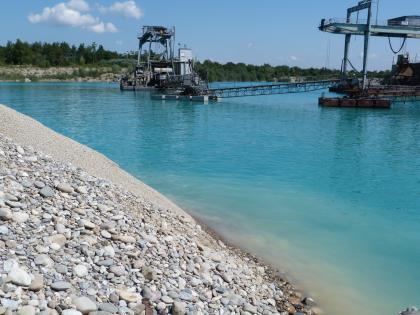 Nassabbau von Kies mit dem Schwimmbagger Das Bild zeigt den Abbau von Kies aus einem See mittels Schwimmbagger. Links vorne schiebt sich ein Kieshang in den See.