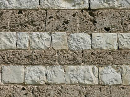 Mauer aus Kalktuffquadern und Bankkalksteinen Nahaufnahme einer Steinmauer, wechselagig gesetzt aus zwei unterschiedlichen Materialien: weißliche schraffierte Blöcke, quadratisch bis rechteckig, sowie größere und kleinere graue Blöcke mit löchriger Oberfläche.