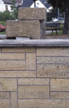 Brunnenstein und Mauerverkleidung aus Tengener Randen-Grobkalk, Rathausvorplatz in Tengen Nahaufnahme einer gelblich grauen Steinmauer mit oben überstehender Krone. Im Hintergrund eine kurze Treppe aus zwei Steinblöcken.