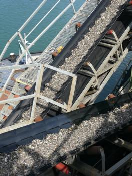 Gewaschene Kieskörnung Blick auf sich kreuzende Förderbänder mit Kiesfüllung. Die Bänder werden über seitliche Rollen bewegt. Links außen verläuft ein Laufgitter.