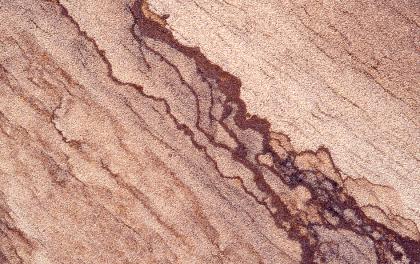 Gelblich brauner Weiler Schilfsandstein mit Limonitbänderung, Fassade der Stuttgarter Staatsgalerie Nahaufnahme einer gelblich braunen Gesteinsoberfläche mit wolkenartigem, schräg von links oben nach rechts unten verlaufendem, rotbraunem Muster.