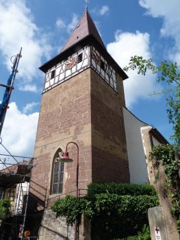 St. Jakobskirche in Brackenheim-Haberschlacht aus Heuchelberger Schilfsandstein Aufwärts gerichteter Blick auf einen hohen, viereckigen Turm aus rötlichem Mauerwerk mit Fachwerkaufsatz unterhalb des spitzen Daches.