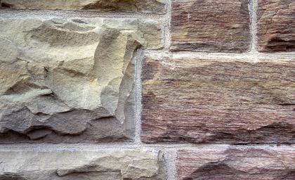 Quader an einem Gasthausgebäude in Bühlertann aus Schilfsandstein Nahaufnahme von gelblichen bis rötlichen Mauersteinen, rechts mit feinen Furchen, links mit Auffaltungen.