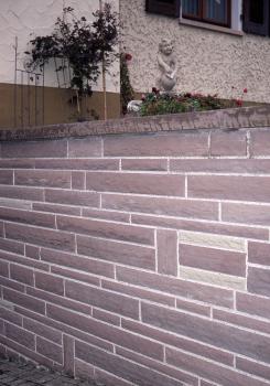 Neue Mauer aus Trichtinger Schilfsandstein, Ortszentrum Trichtingen Teilansicht einer rötlich grauen Steinmauer, die quer zu Hauswänden steht.