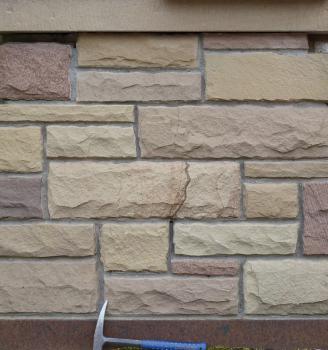 Nahaufnahme von Mauersteinen in unterschiedlichen Farben und Formen. Ein Hammer am unteren Bildrand dient als Größenvergleich.