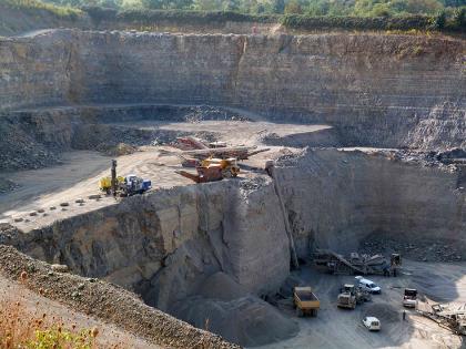 Kalksteingewinnung im Steinbruch Knittlingen-Bretten Blick von oben in einen abgestuften Steinbruch. Rechts unten ist der Boden sichtbar, mit Lastwagen und Radlader. Nach links hin steigt eine höhere Sohle auf, ebenfalls mit Fördergeräten, zum Hintergrund eine noch höhere Bruchwand.