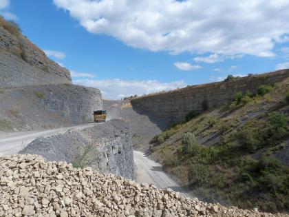 Räumlich beengte Abbausituation im Steinbruch Vaihingen an der Enz-Roßwag Blick auf die eng stehenden seitlichen Wände in einem Steinbruch. Links sind die Sohlen terrassiert, rechts ragt ein bewachsener Hang ins Bild. Im Vordergrund befindet sich ein Geröllhaufen.