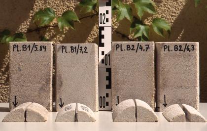 Bohrkernabschnitte im Stubensandstein bei der Burkhardtsmühle Das Foto zeigt vier nebeneinander aufgestellte, rötlich graue Gesteinsblöcke mit Beschriftungen. Davor liegen gerundete Gesteinskerne, teils in Viertel geschnitten.