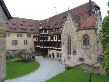 Coburger Veste, erbaut aus Burgsandstein Blick auf einen mittelalterlich wirkenden Gebäudekomplex mit Eckhaus, Fachwerkhaus und Kapelle. Alle Gebäude sind aus grauem bis hellbraunem Mauerwerk errichtet, haben rote Dächer und sind um einen gepflasterten sowie begrünten Innenhof gruppiert.