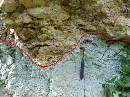Erosionsdiskordanz zwischen Sandstein (oben) und Tonstein Teilansicht von zweigeteiltem Gestein: Oben grünlich braun mit hervortretenden Blocksteinen, darunter bläulich grau und knollig bis schrundig. Eine hinzugefügte rote Trennlinie markiert beide Bereiche.