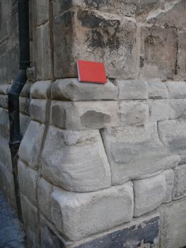 Mauerquader an der Kirche St. Johannis in Schwäbisch Gmünd aus Stubensandstein Teilansicht eines Gebäudesockels aus großen grauen, teils abgerundeten Mauerquadern. Ein zwischen Sockel und anschließendem Mauerwerk aufgelegtes rotes Buch dient als Größenvergleich.