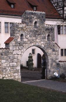 Schloss Hellenstein bei Heidenheim an der Brenz Blick auf einen steinernen Torbogen mit Stufengiebel, drei Fensteröffnungen und aufgelegten Ziegeln. Das Gestein des Tores ist hellgrau bis dunkelgrau. Hinter dem Tor steht ein größeres, weiß verputztes Gebäude.