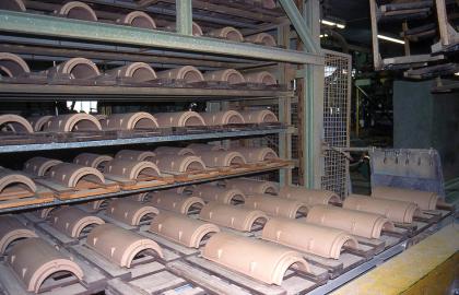 Ehemalige Dachziegelproduktion im heute stillgelegten Werk Mühlacker Das Bild zeigt zahlreiche halbrunde, rötlich braune Dachziegel, die in einem Metallregal gelagert sind.