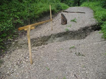 Einfache Messeinrichtung (Messlehre) zum Feststellen von Bewegungen Einfaches, aus Holzlatten gebautes Messinstrument, mit dem ein entstandener Querriss auf einem Kiesweg überbrückt und vermessen wird.