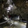 Blick in das Innere einer Höhle. Ein schwach beleuchteter Laufgang mit seitlichen Brüstungen führt im Zickzack durch die Höhle. Eine Wand oberhalb der Bildmitte ist ebenfalls schwach erhellt.