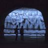 Blick durch einen Tunnel auf eine großformatige, aus Stein gehauene Figurengruppe, die von bläulichem Licht erhellt wird.