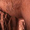 Blick auf Wände und Decke in einem Bergwerksstollen. Im rötlich braunen Gestein sind oben deutliche Spuren von Bearbeitung mit Werkzeugen zu erkennen.