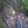 Blick auf einen nach links aufsteigenden Waldhang mit offenliegendem Gestein, auf dessen Oberfläche zahlreiche Steine verbacken sind. Ein Mann in gestreiftem Hemd begutachtet die Steine.