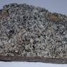 Nahaufnahme eines Handstückes von Sankt Blasien-Granit. Das Stück ist länglich rechteckig und grau mit dunkleren Einsprenglingen.