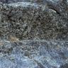 Teilansicht von bläulich grauem, leicht gestuftem Felsgestein. Über der Bildmitte sind zahlreiche kleine Löcher im Fels zu erkennen.