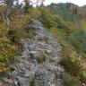 Blick auf einen treppenartigen, aufwärts führenden Felsenweg, der scheinbar neben einem Baum endet. Im Hintergrund rechts ein bewaldeter Berg.