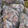 Blick auf mehrere hinter- und übereinanderliegende Gesteinsblöcke. Das graue, teils von rötlichen Schlieren durchzogene Gestein zeigt Risse und Klüfte.