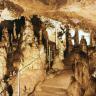 Blick in das Innere einer Höhle. Entlang eines aufwärts führenden, mit Halteseilen gesicherten Weges sind zahlreiche, vom Boden zur Decke wachsende Tropfsteinsäulen zu sehen.