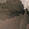 Teilansicht einer Höhle mit dünnplattigen, scharfkantigen Zwischenwänden vor der eigentlichen Höhlenwand. Auch von der Decke hängen dünne Plattenbildungen herab.